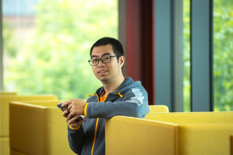 international student standing next to a chair on their phone